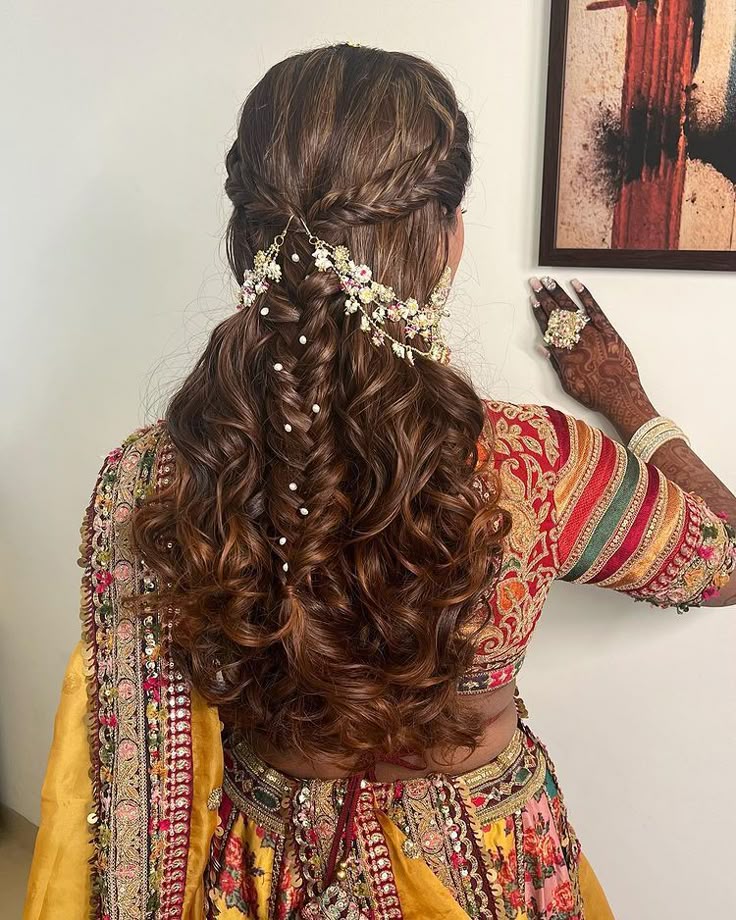 Half-up braided bridal hairstyle with soft curls, floral accessories, and pearl embellishments, perfect for Jaago or Mehendi functions.