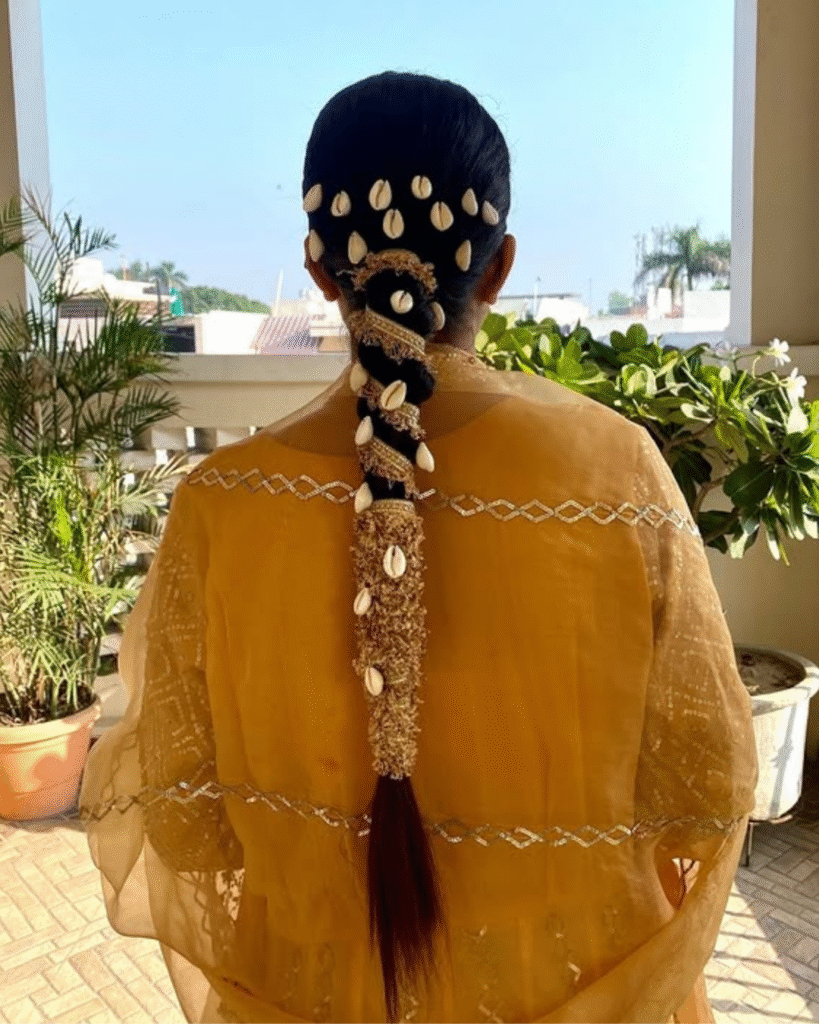 Traditional Jaago hairstyle featuring a sleek braid adorned with cowrie shells and golden accessories