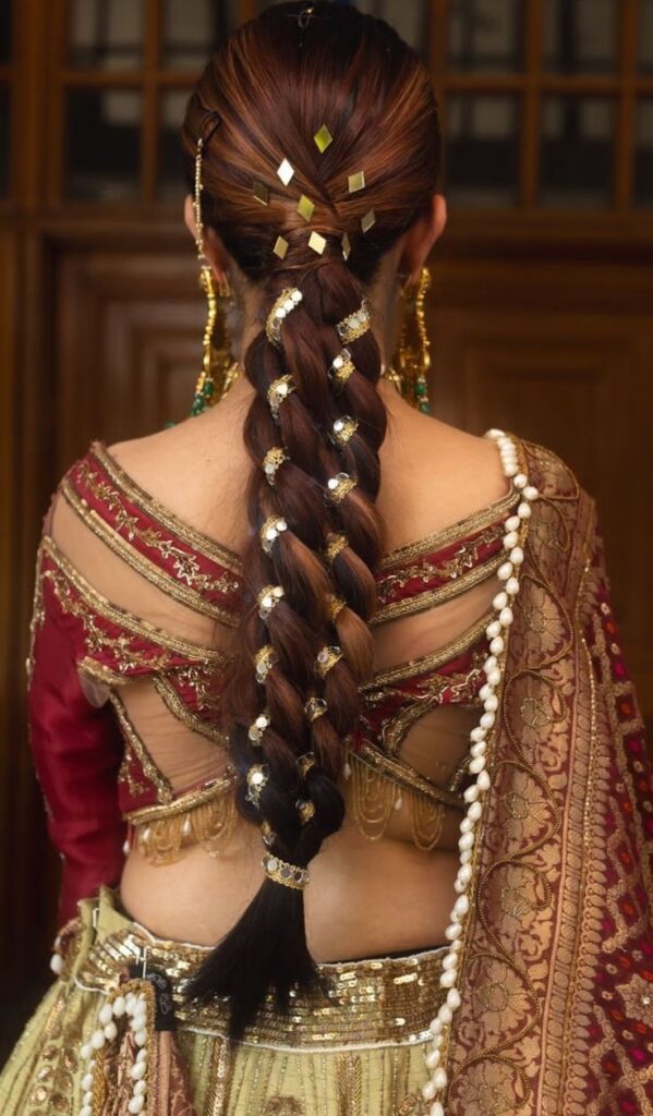 Elegant braided hairstyle featuring golden hair accessories and diamond-shaped embellishments, paired with a heavily embroidered blouse and lehenga for a festive Jaago night look.