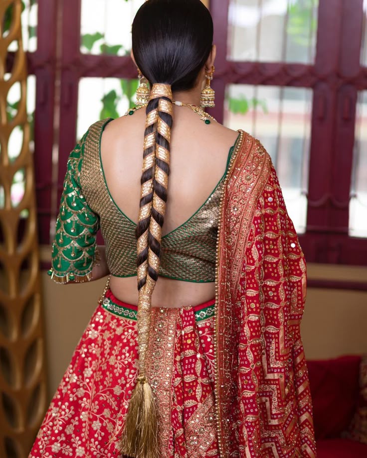 Traditional bridal braid wrapped in shimmering gold accessories and finished with a bold golden tassel, worn with a green and red lehenga set—perfect for Jaago or wedding festivities.