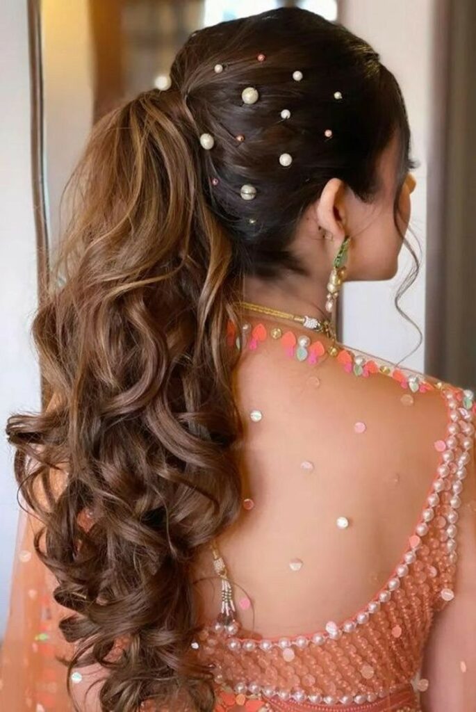 Bridal ponytail hairstyle with voluminous curls, decorated with pearl hairpins — perfect for Punjabi Jaago or Sangeet night