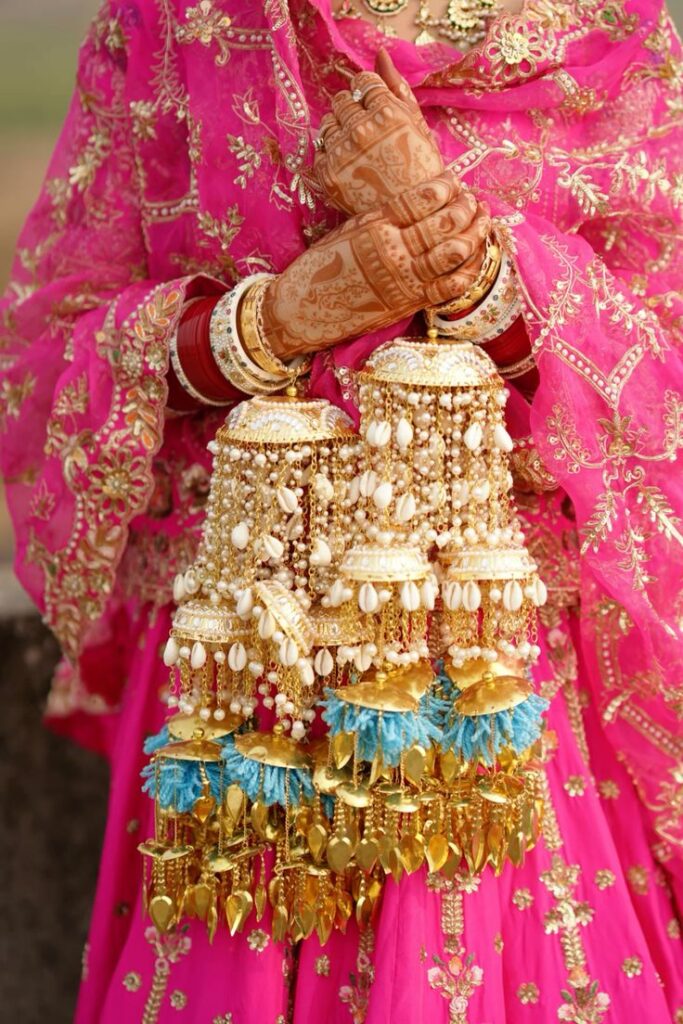 Punjabi bride wearing custom kaleere with pearls, shells, and blue embellishments over pink bridal lehenga