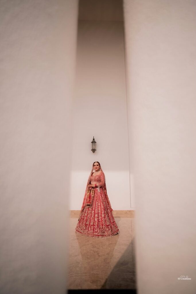 Bride in red Seema Gujral lehenga framed by architectural pillars before her sunset Punjabi wedding